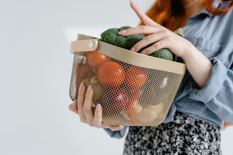 A Person Carrying  Steel Basket With Assorted Fruits And Vegetables