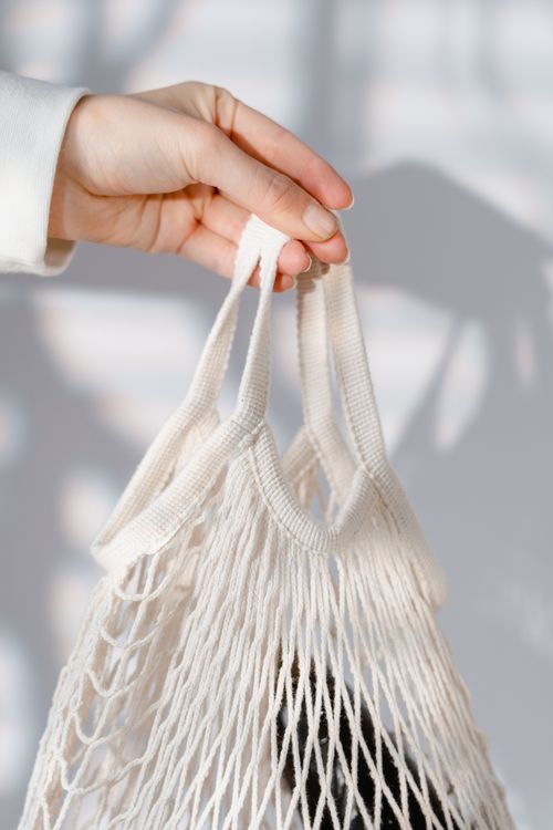 Free Close-up of a hand holding a white mesh bag in bright sunlight with shadows. Stock Photo