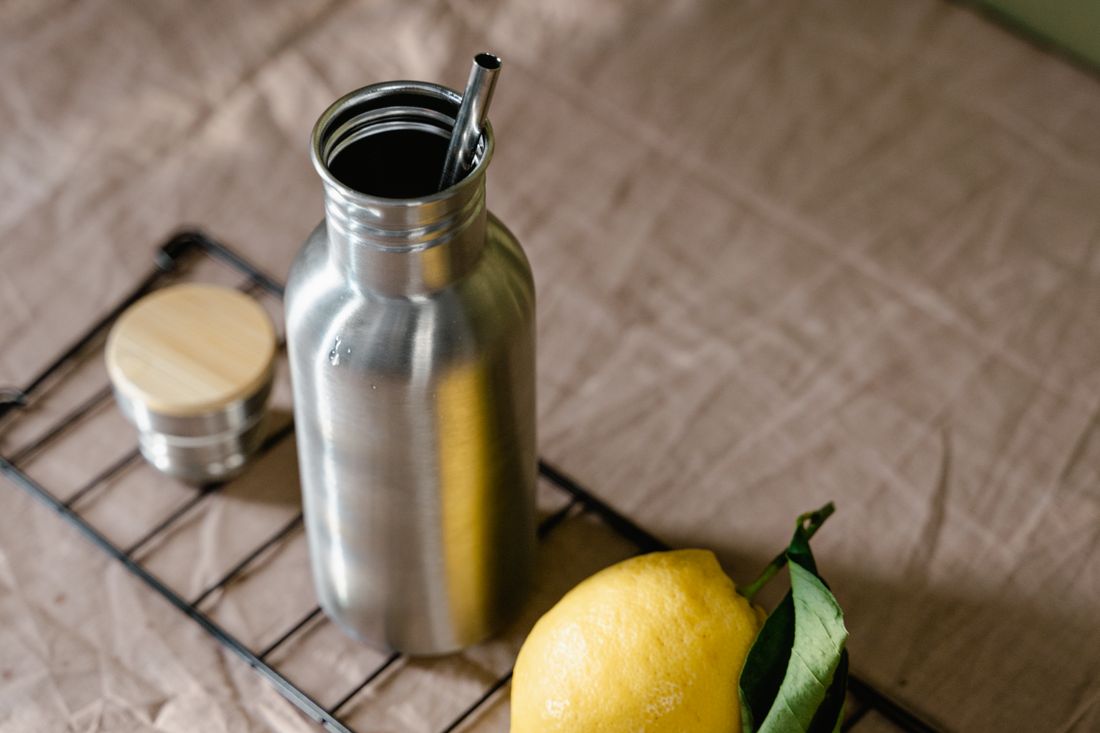 Steel water bottle with a straw lid next to a lemon