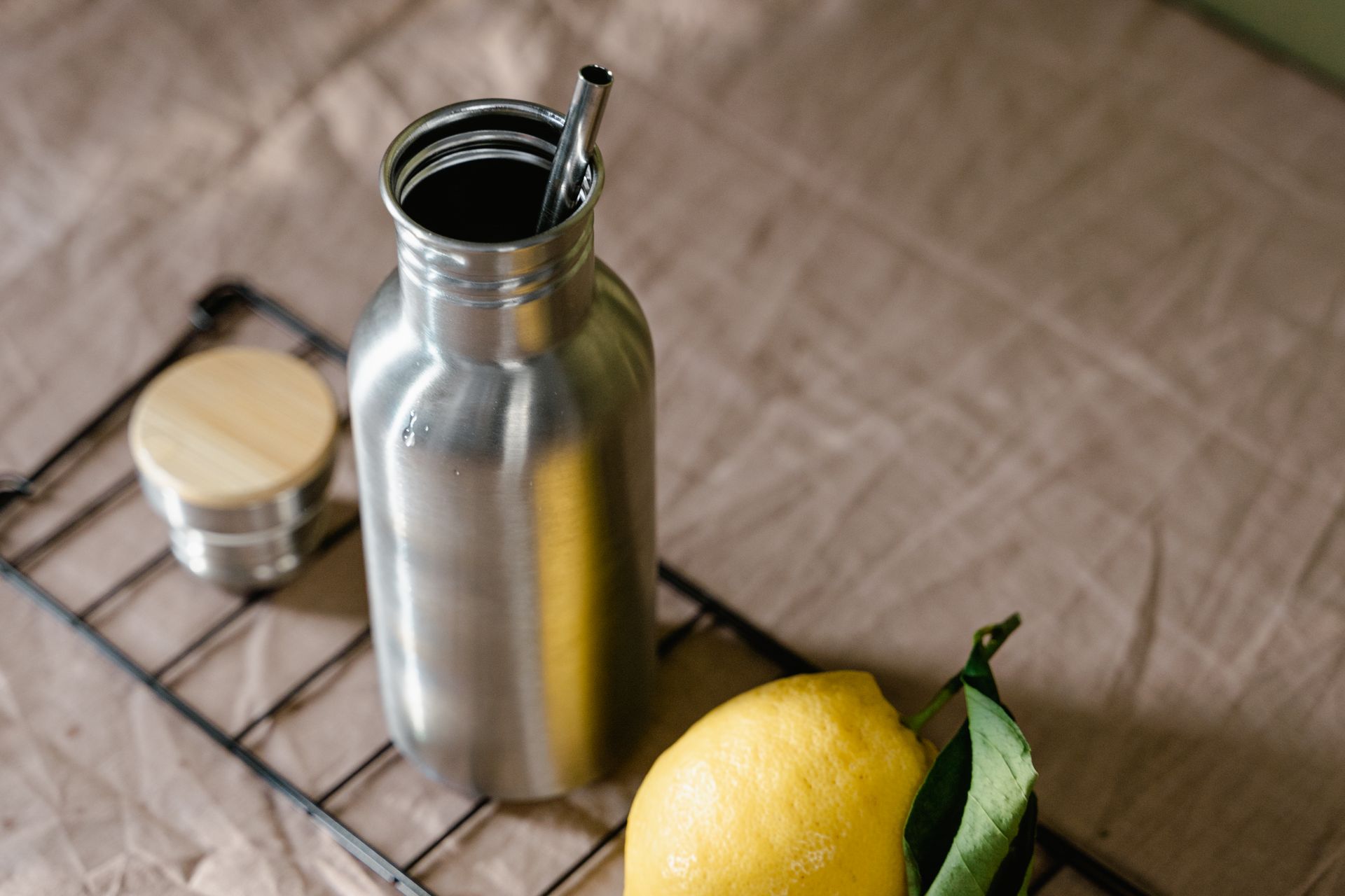 Eco-friendly metal bottle with lemon and reusable straw on natural fabric.