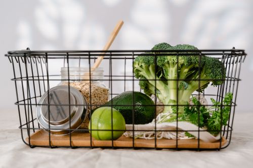 Free A wire basket holds fresh broccoli, lime, avocado, oats in a jar, and leafy greens. Stock Photo