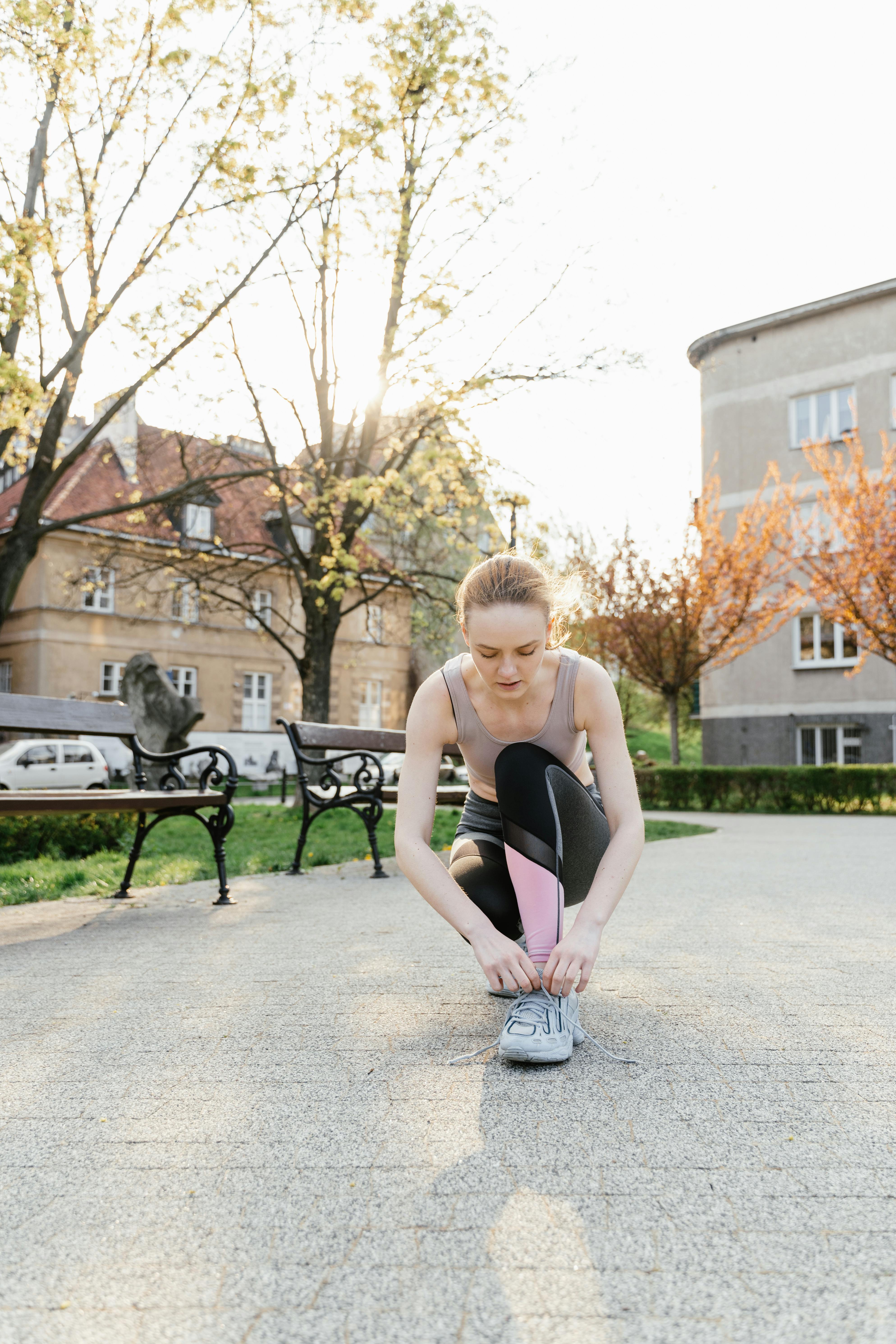 Woman smiling, tying running shoes, bright morning light, park path, fitness journey start.