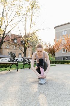 A woman tying her shoes in a park, getting ready for exercise on a sunny day.