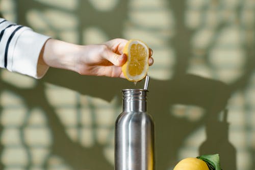 A Person Squeezing Lemon on Stainless Bottle