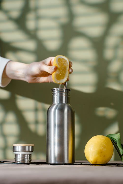 A Person Squeezing a Slice of Lemon in a Stainless Steel Tumbler