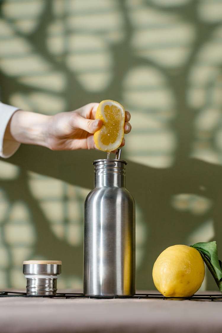 A Person Squeezing A Slice Of Lemon In A Stainless Steel Tumbler