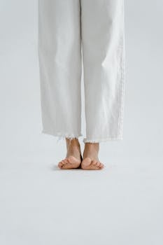 Close-up of a person standing barefoot with white jeans in a minimalist setting.