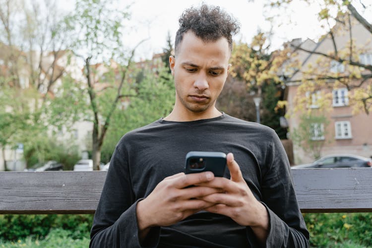 Man Sitting Outdoors Texting On A Smartphone 