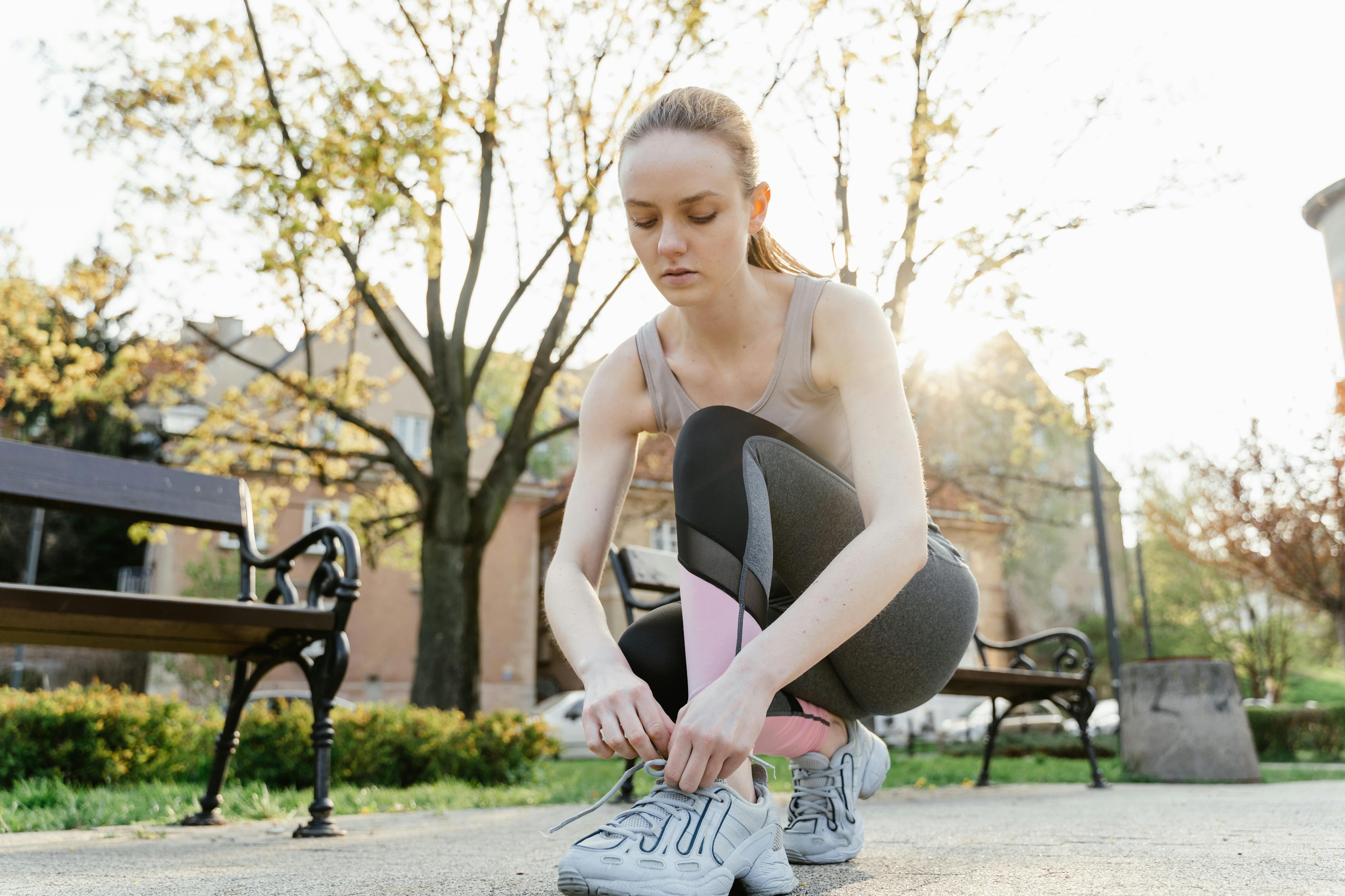 Woman tying shoes before workout in sunny park; fitness and wellness concept.