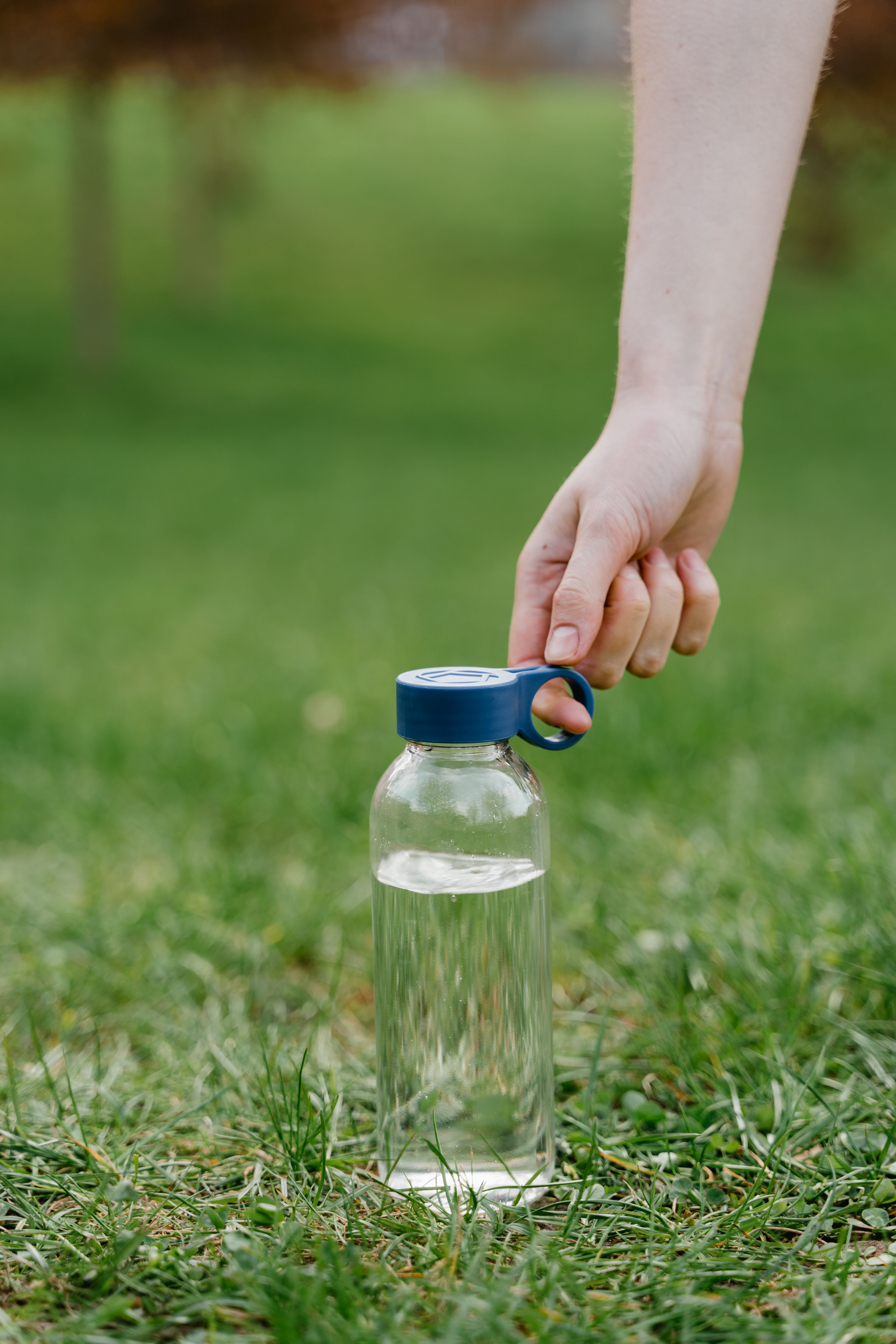A hand holding a water bottle with a blue lid on green grass outdoors, ideal for hydration themes.