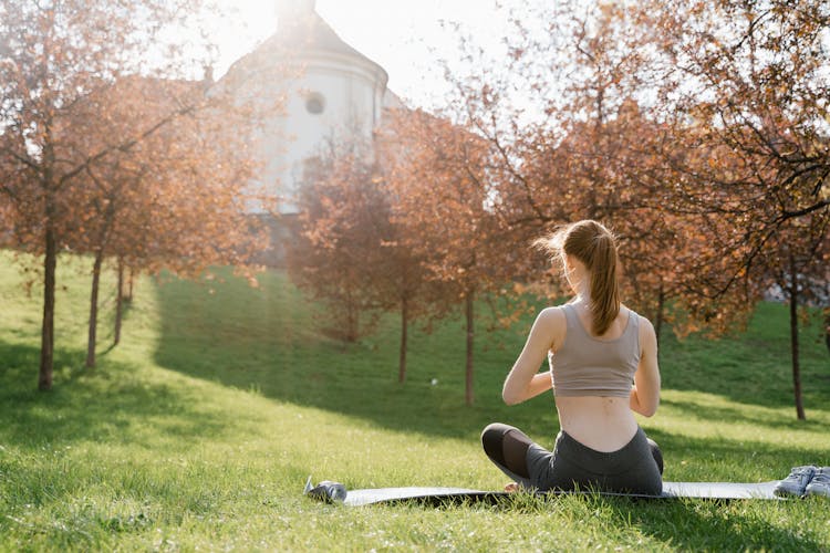 Back View Of A Woman Meditating At A Park