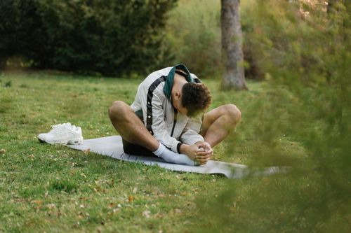 Free Male athlete stretching on a yoga mat in a serene outdoor park setting, promoting fitness and relaxation. Stock Photo