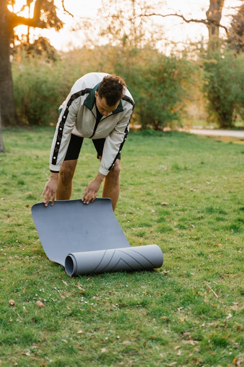 A Man Rolling Out a Yoga Mat at a Park