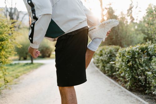 Free Close-up of a person stretching leg in a sunny outdoor park, ideal for fitness themes. Stock Photo
