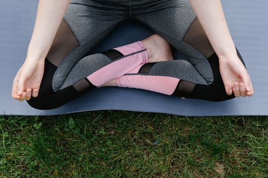 Person meditating in yoga pose on a mat in a grassy outdoor setting.