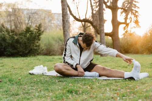 Free A man performs stretching exercises on a yoga mat in a sunny park. Stock Photo