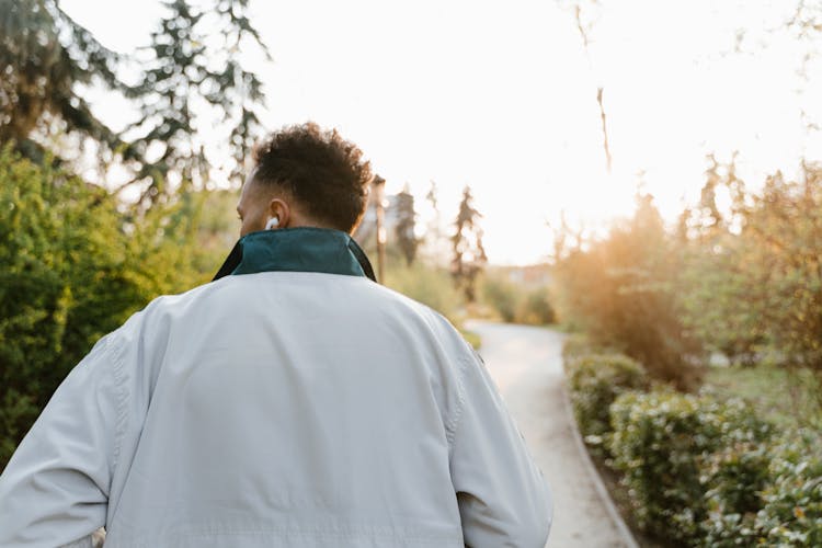 A Back View Of A Man In A Jacket Walking At A Park