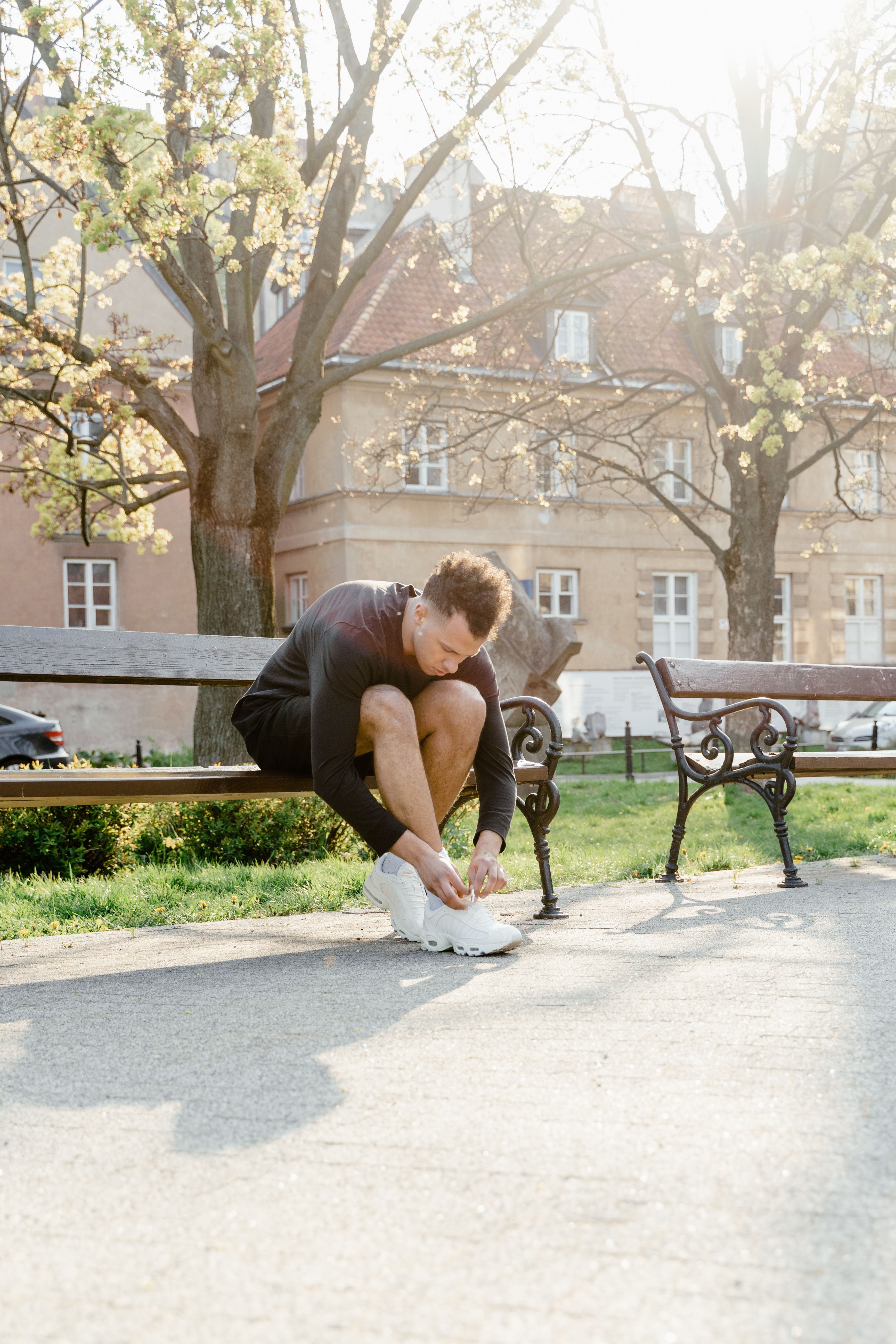 Man in athletic wear ties shoes outdoors on a sunny day in a park.