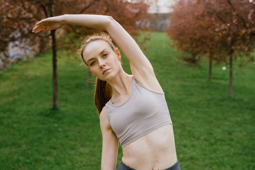 An athletic woman stretches in a green park; promoting outdoor fitness and wellness.