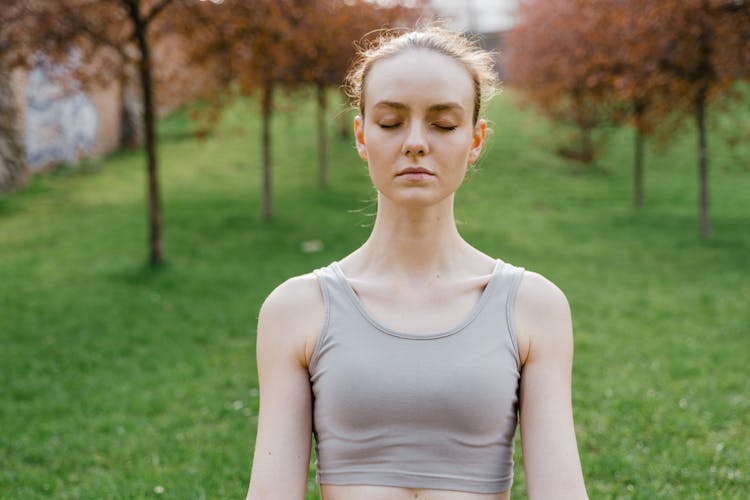 Young Woman In A Sports Bra Standing Outside With Eyes Closed