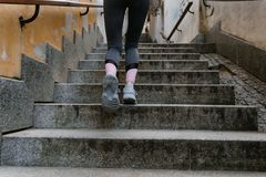 Woman in athletic gear jogging up an outdoor stone staircase during the day.