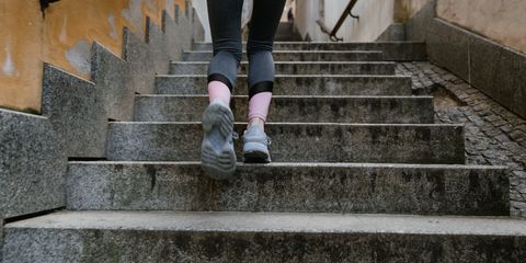 Woman in athletic gear jogging up an outdoor stone staircase during the day.