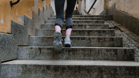 Woman in athletic gear jogging up an outdoor stone staircase during the day.