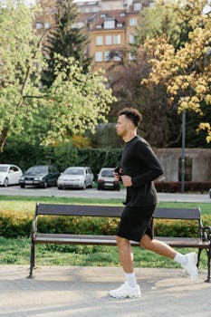 Man jogging in a vibrant urban park, flanked by benches and trees, enjoying a peaceful workout.