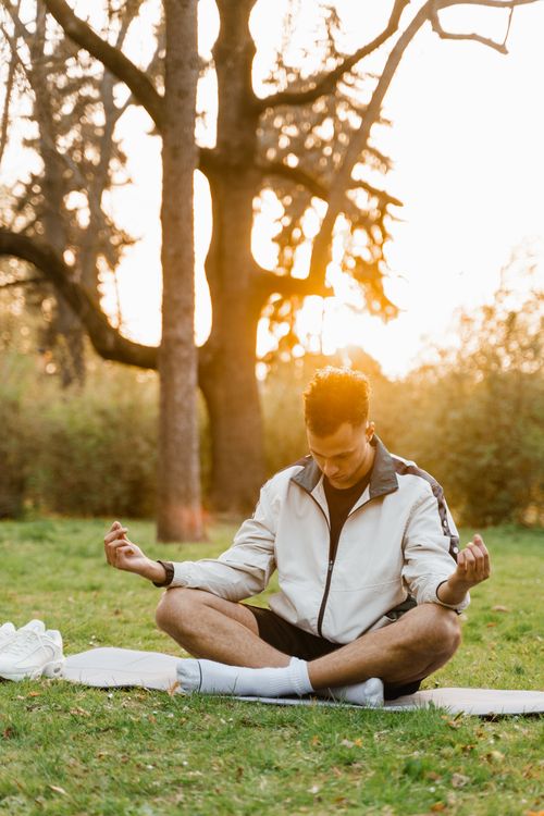 Free A young man meditates on a yoga mat in a serene park during sunset. Stock Photo