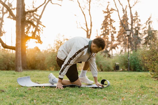 A man unfolds a yoga mat in a park during sunrise, embracing a healthy outdoor lifestyle.