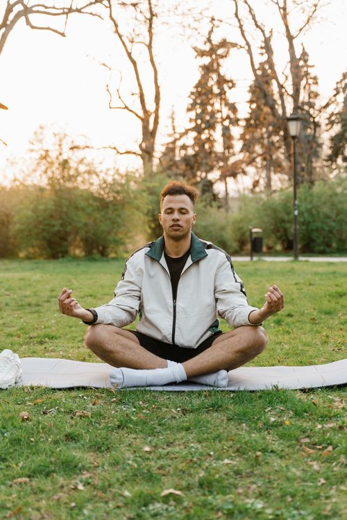 Free Young man in lotus pose meditating outdoors on a yoga mat at sunset, promoting relaxation and wellness. Stock Photo