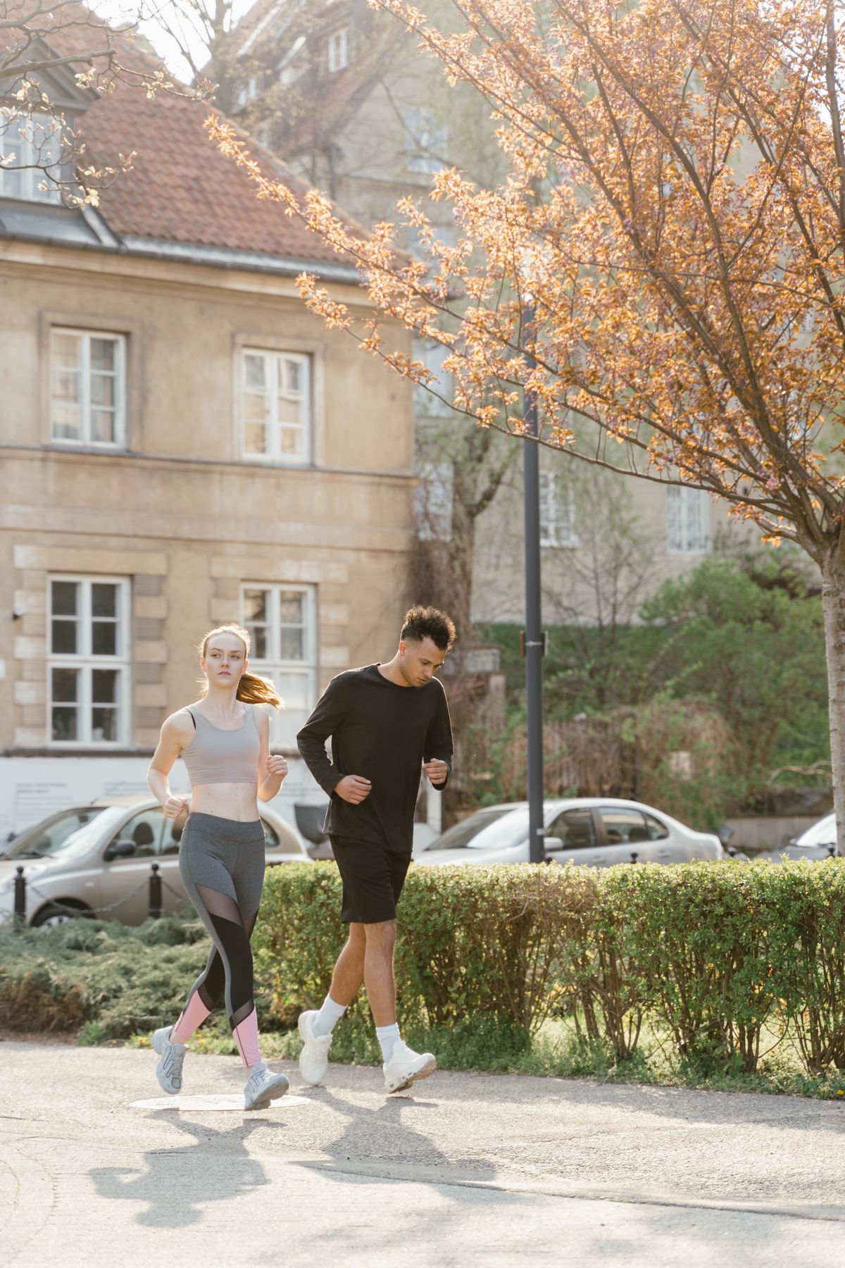 Two runners jogging side by side through a sunlit park at a relaxed, conversational pace