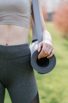 Woman holding a rolled yoga mat outdoors, ready for exercise in nature.