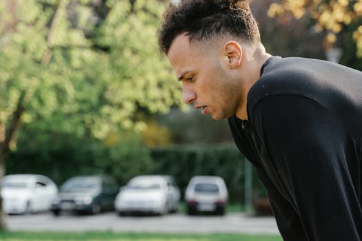 A man in black clothing takes a break after outdoor exercise, looking tired.