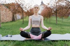 A woman performs meditation in a serene park setting on a yoga mat.