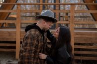 Side view of smiling young couple in trendy autumn clothes near wooden building cuddling while standing close in street and looking at each other