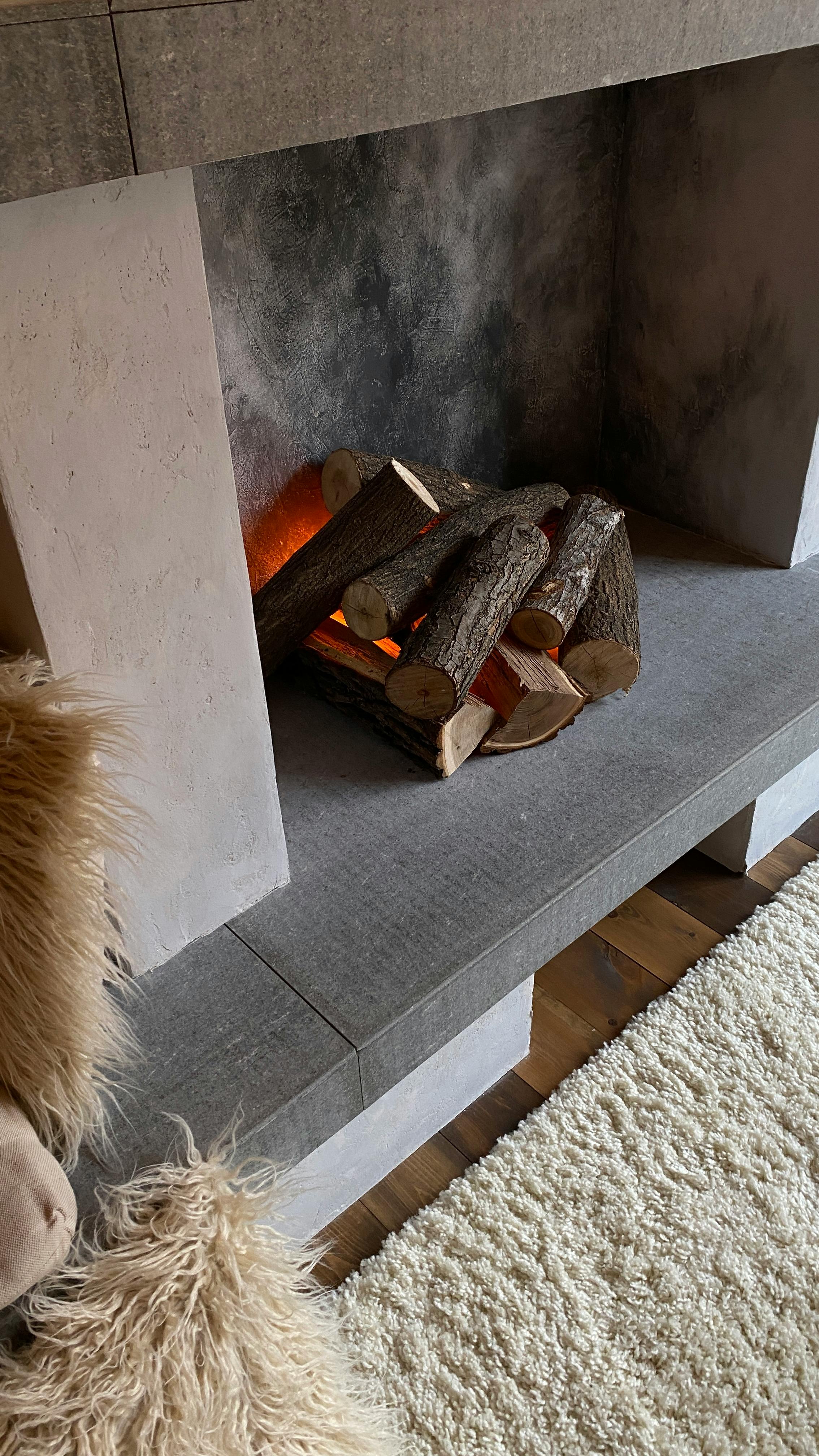 From above of soft carpet placed near fireplace with burning woods in cozy room