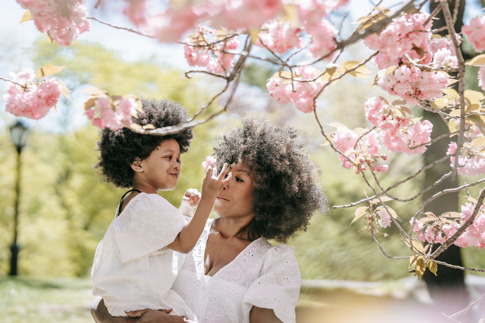A mother and daughter share a joyful moment under blooming cherry blossoms in a park during the day.