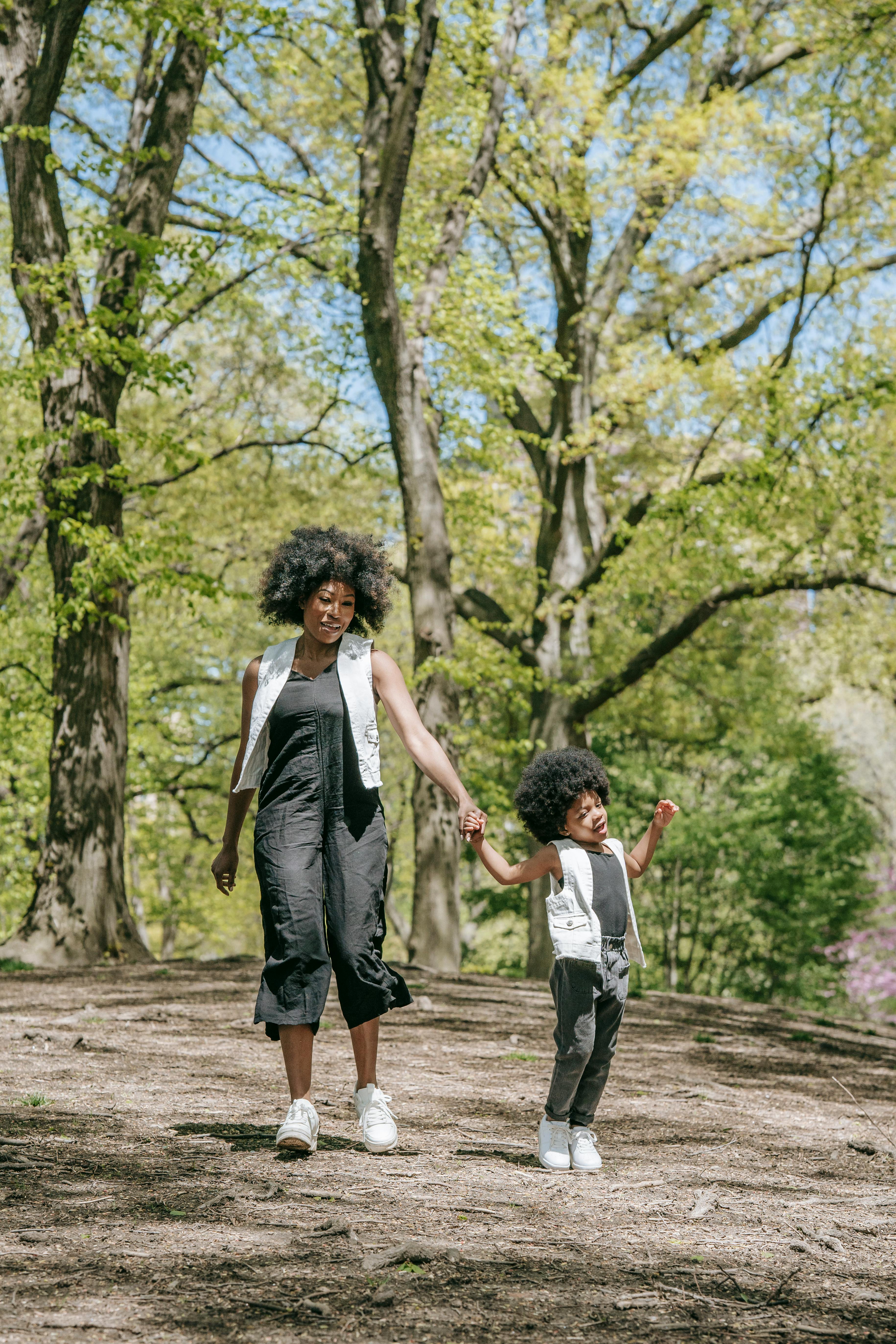 A joyful mother and child with afro hair walking hand in hand in a green park during spring.