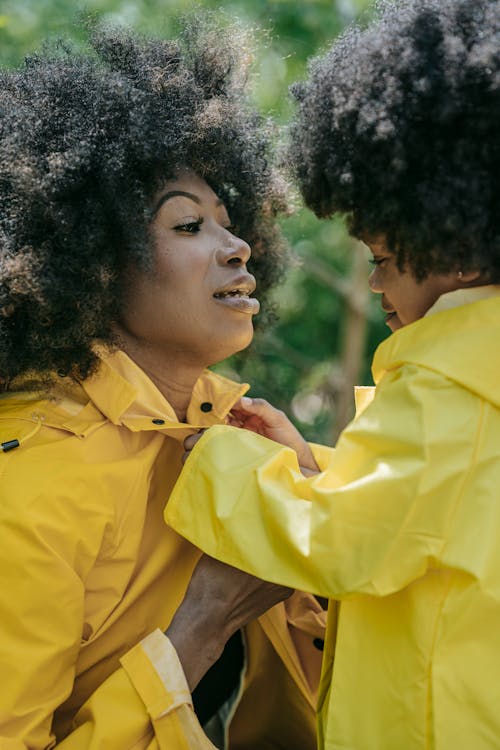 A Young Girl Putting Buttons on a Woman's Raincoat
