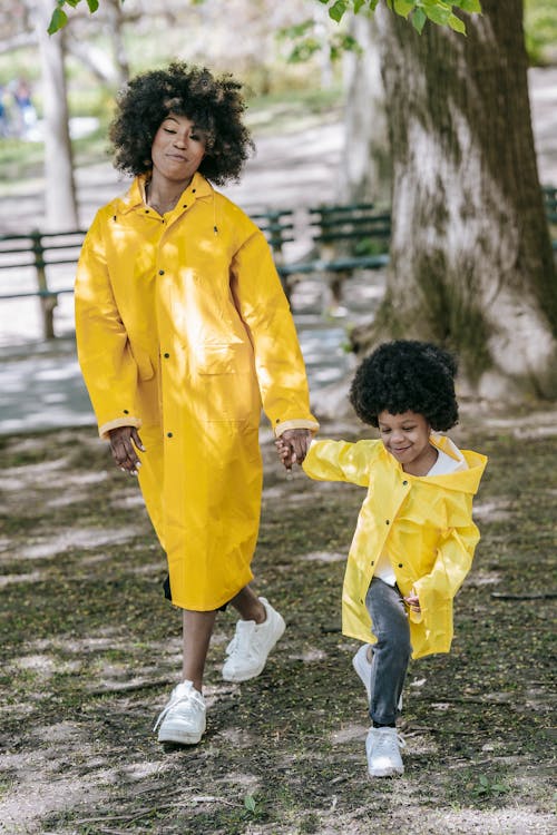 A Woman and a Child with Matching Raincoats Walking at a Park