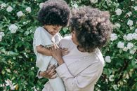 Woman in White Long Sleeve Shirt Carrying Baby in White Dress