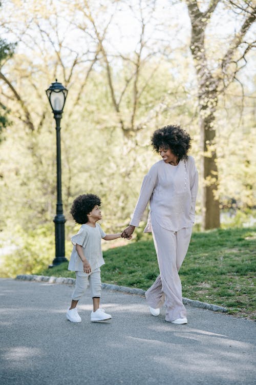 A Woman and a Child Walking on the Concrete Pavement at the PArk