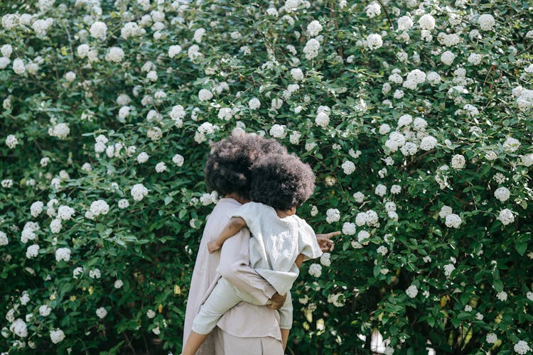 Mother With Daughter By Flowering Shrubs