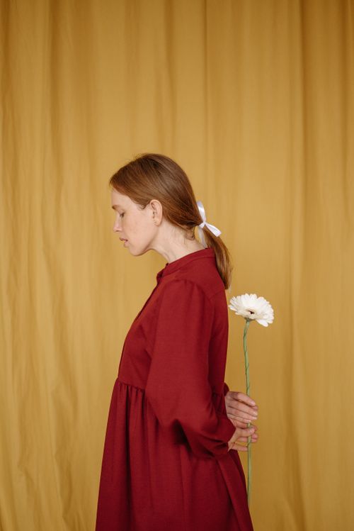 Free A woman in a red dress poses with a flower against a yellow curtain in a studio setting. Stock Photo