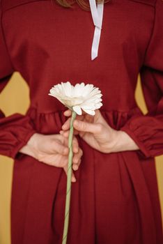 Close-up of a woman in a red dress holding a white gerbera behind her back.