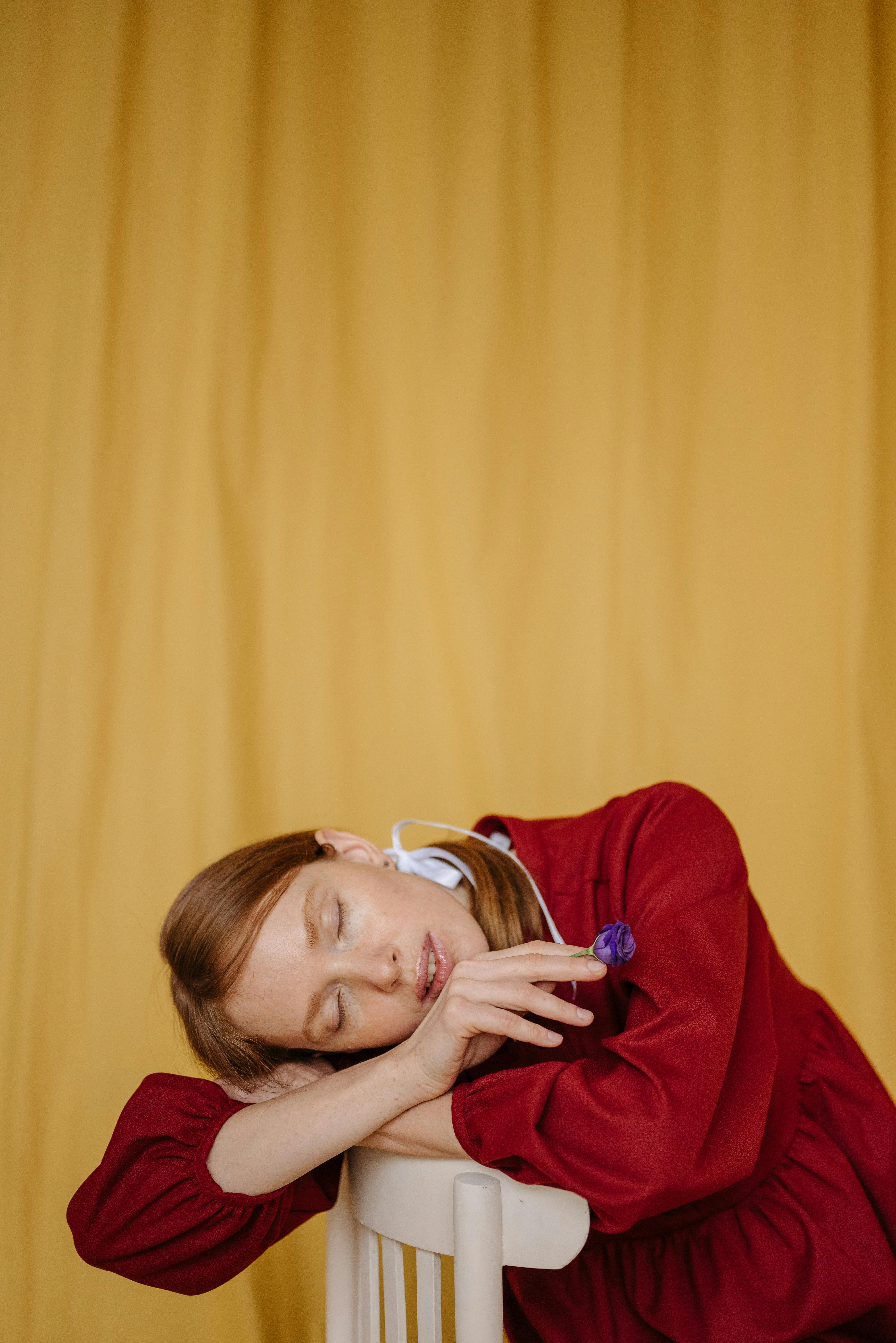 Portrait of a woman resting on a chair in a studio with a yellow background.