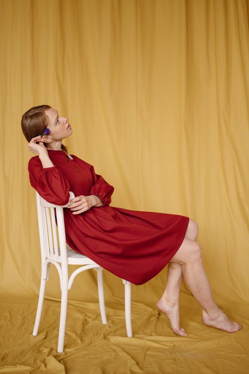 Free A woman in a red dress sits gracefully on a white chair against a yellow backdrop. Stock Photo