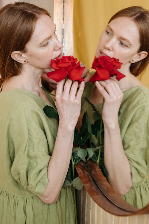 A Woman Holding Red Flower in Front of Mirror