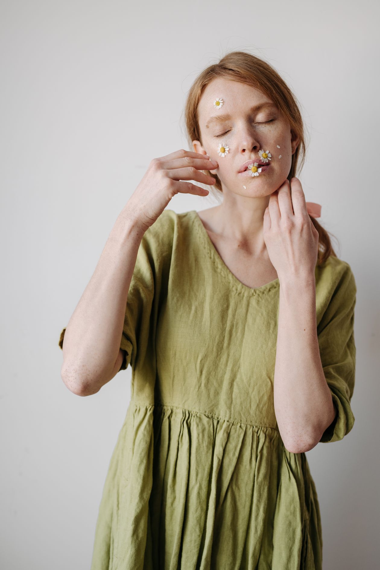 Woman in an olive green linen dress with daisies on her cheeks